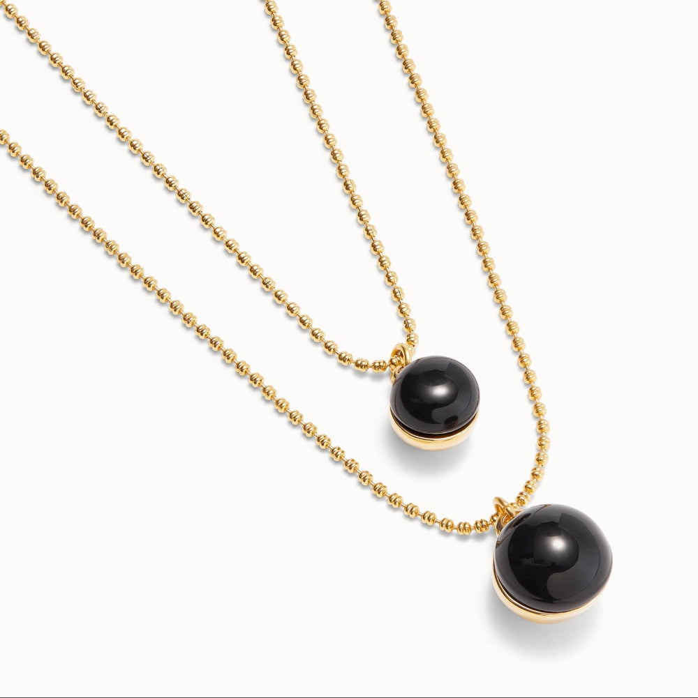 Two gold-tone beaded chain necklaces with spherical black pendants, one small and one larger, displayed on a clean white background.