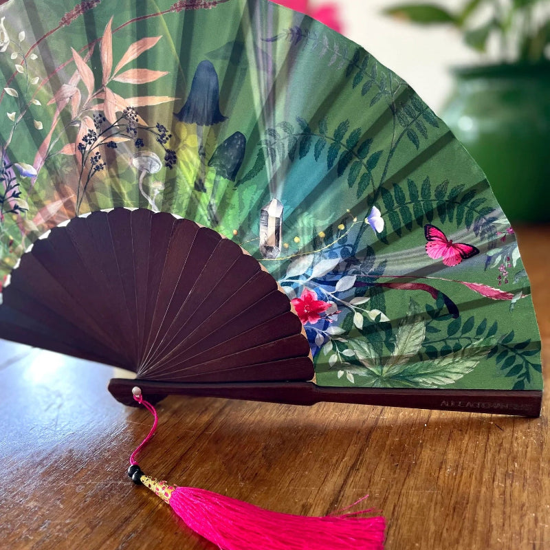 Decorative fan with floral design on a wooden surface with pink flowers in the background