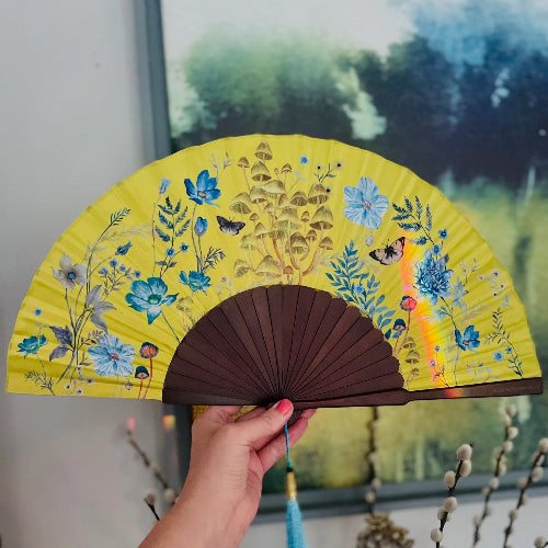 Hand holding a decorative fan with floral design against a blurred background