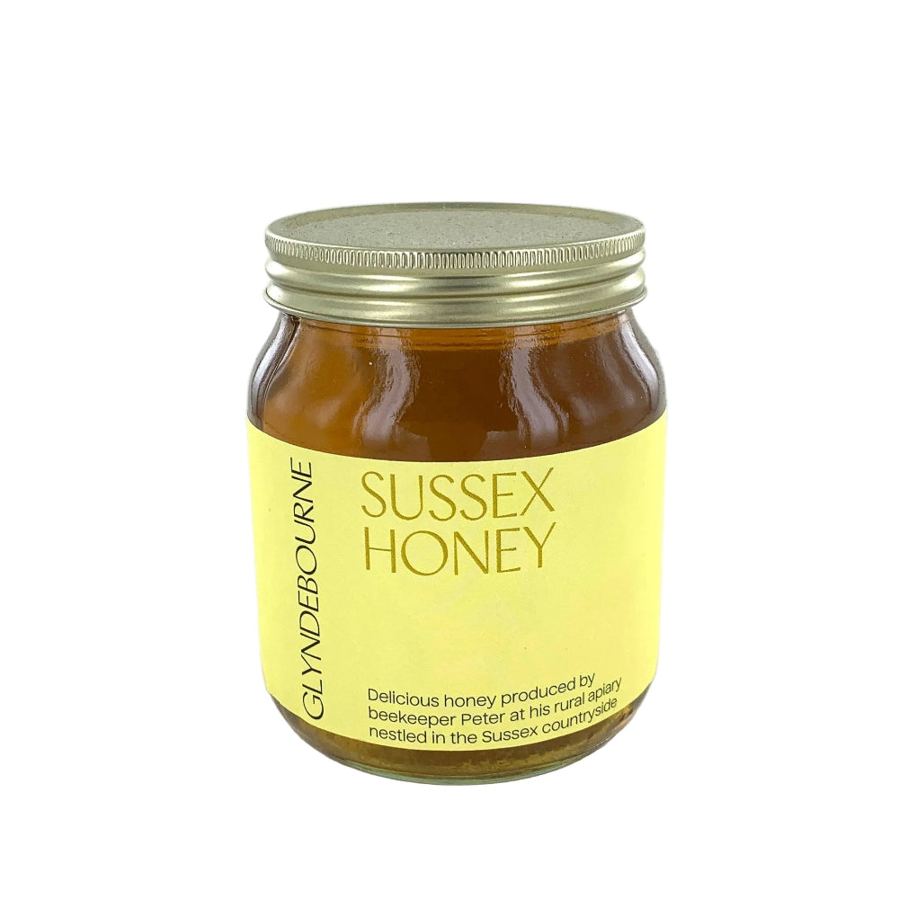 A glass jar of Glyndbourne Sussex Honey with a yellow label and a gold metal lid, set against a plain white background.