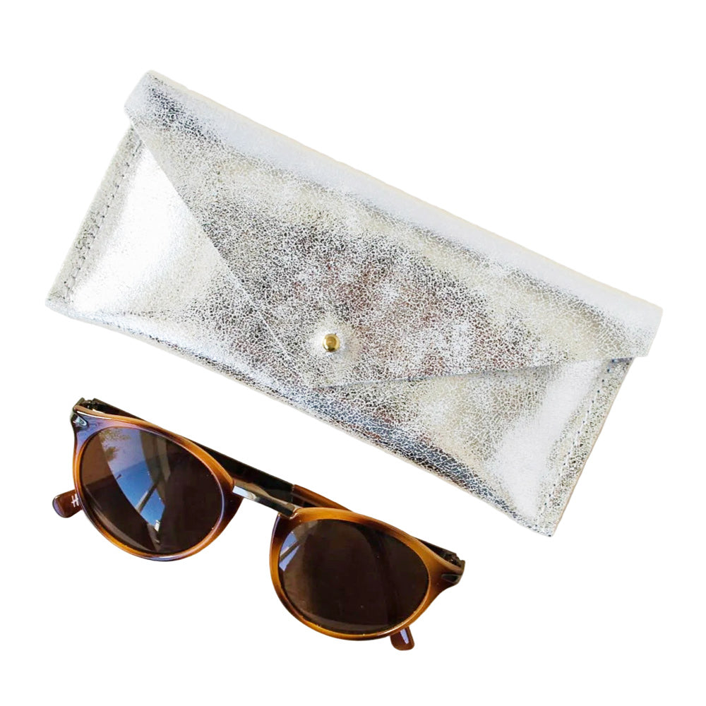 A pair of round sunglasses with brown frames and dark lenses, displayed next to a metallic silver envelope-style case on a plain white background.