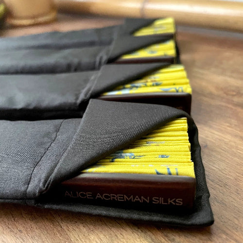 Black silk scarf with yellow pattern inside a black case on a wooden surface, branded 'Alice Acreman Silks'.