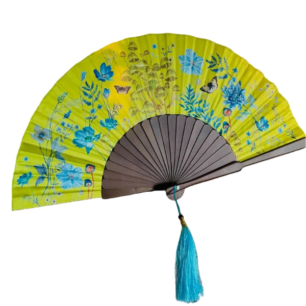 Yellow floral fan with a blue tassel on a wooden surface, with a blurred background.